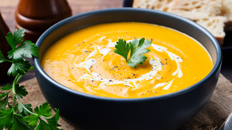Bowl of carrot soup drizzled with heavy cream and garnished with parsley