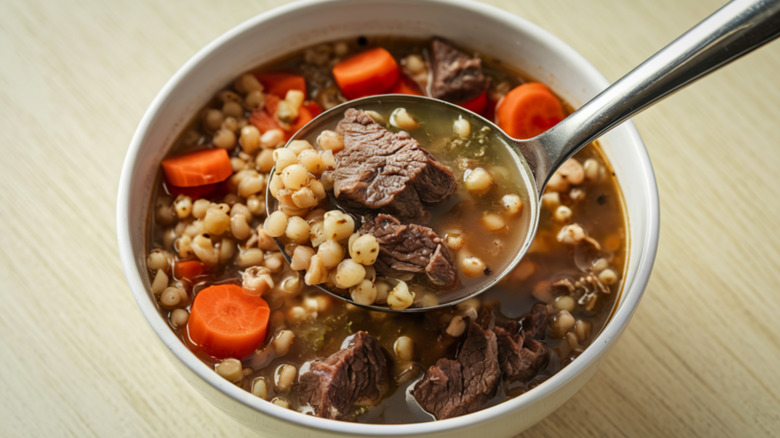 Spooning beef and barley soup from a bowl