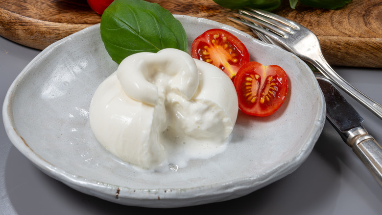 Ball of burrata cheese in dish with tomato and basil leaf