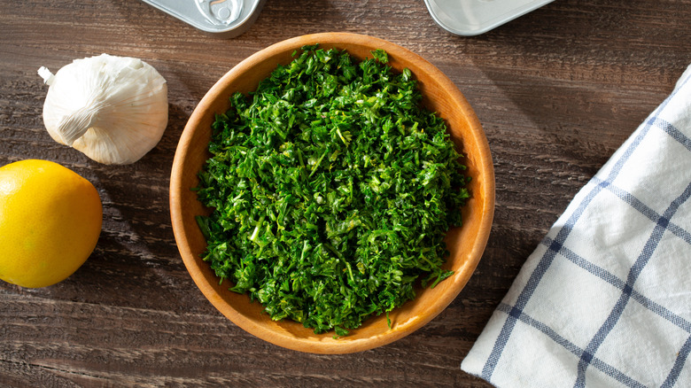 Bowl of herb gremolata next to lemon and bulb of garlic and a lemon