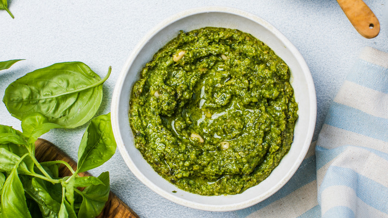 Bowl of pesto sauce next to spinach and basil leaves