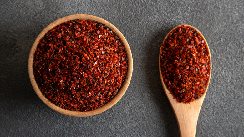 Red pepper flakes in wooden bowl and on wooden spoon