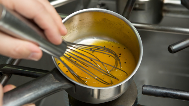 hand whisking as a small quantity of chicken broth reduces over a gas stove