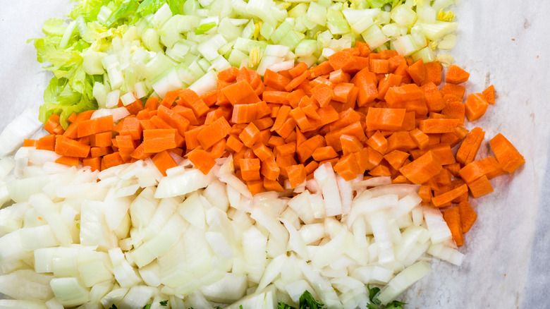 classic mirepoix of onions, carrot and celery on a white work surface