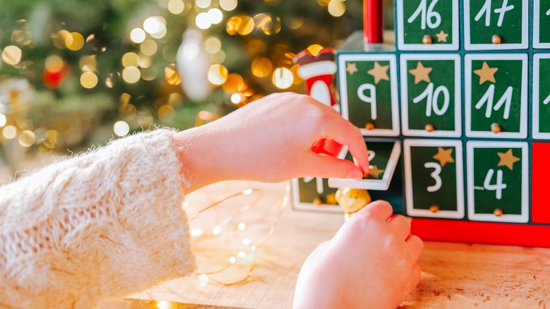 hands opening the door of an advent calendar and removing a gold bear