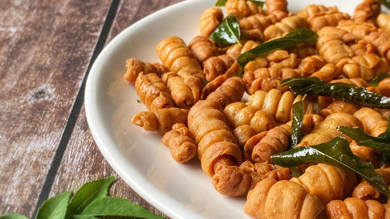 Kuih siput snacks on a plate with fried curry leaves