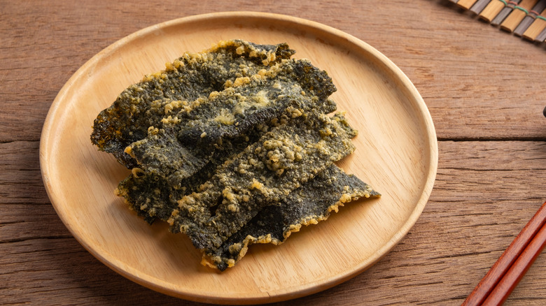 Fried tempura seaweed chips on a wooden plate on a wooden table with chopsticks