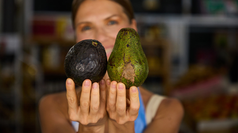 Woman holding two different colored avocados