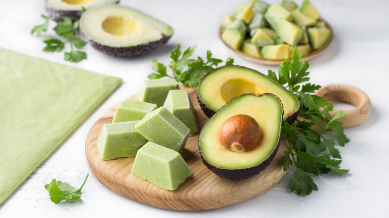 Frozen chunks of mashed avocado next to a fresh avocado