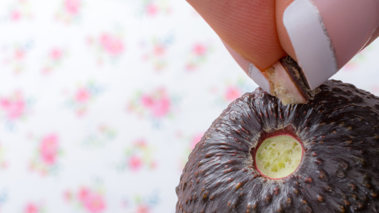 Woman's fingers pulling back and avocado stem to reveal green flesh