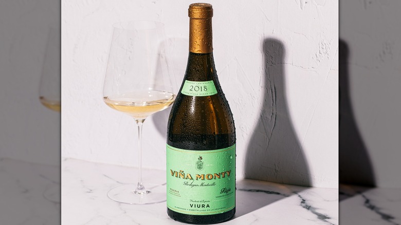 Bottle of Viura Reserva 2018 next to a glass of wine on a marble tabletop