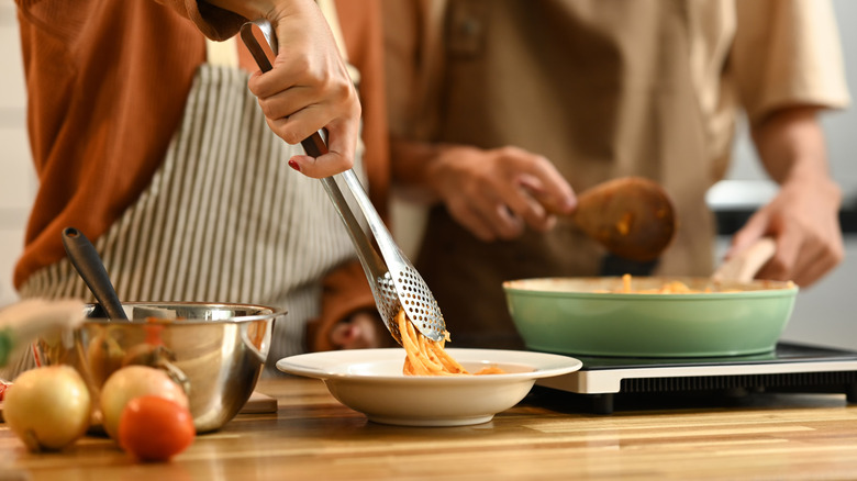 woman putting pasta into a bowl with person in the background