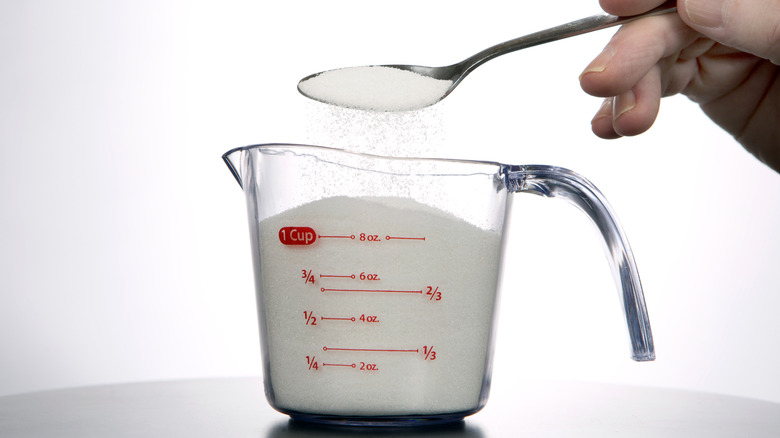 measuring spoon with sugar spooning into measuring cup of sugar