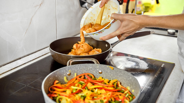 woman adding chicken to a skillet with skillet of vegetables alongside