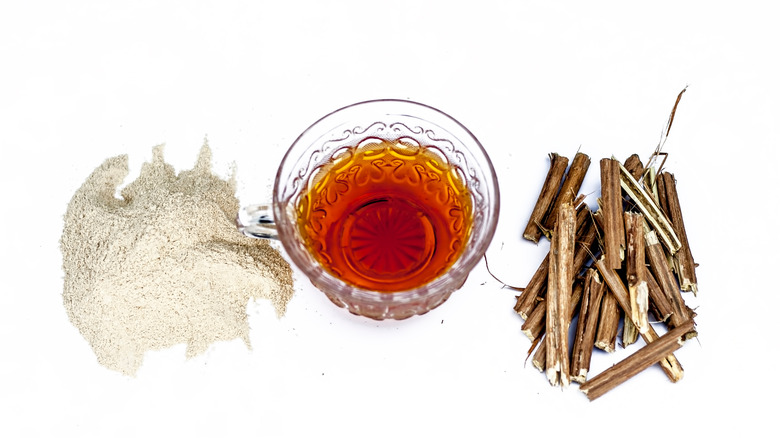 Cup of ashwagandha tea surrounded by ashwagandha roots and powder on white background