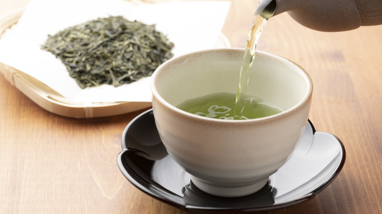 Cup of green tea with bowl of green tea leaves on a wooden table
