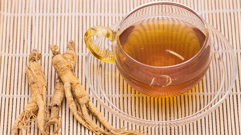 A cup of ginseng tea placed next to ginseng roots on wooden placemat