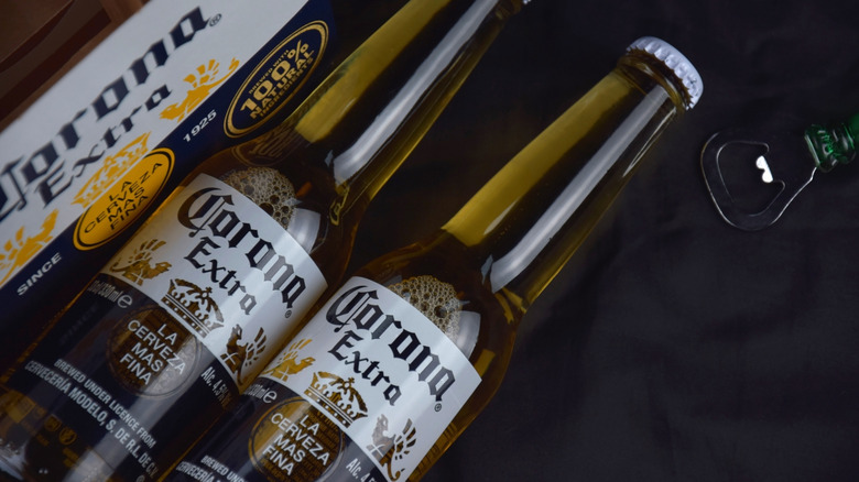 Two bottles of Corona Extra laid down with a branded carrier and bottle opener
