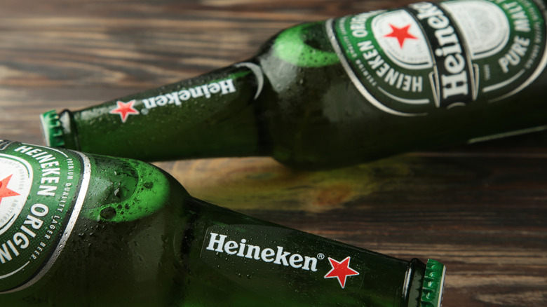 Two bottles of Heineken laid down horizonally on a wooden table in opposite directions