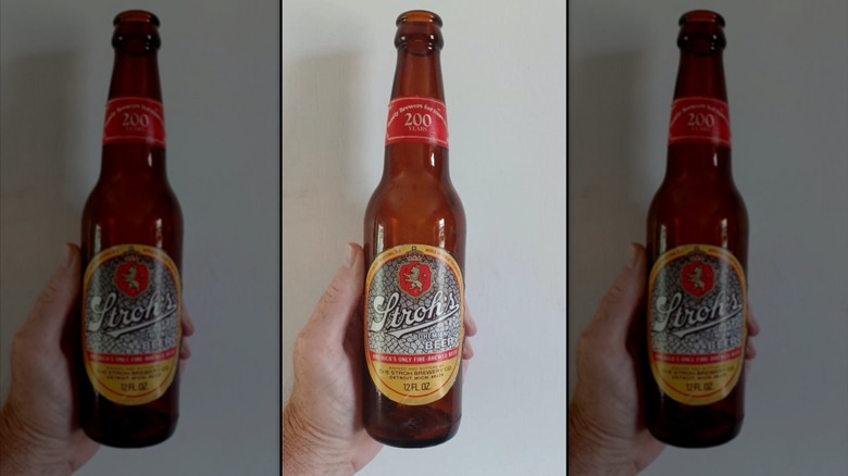 hand holding Stroh's beer bottle against white wall, mirrored image
