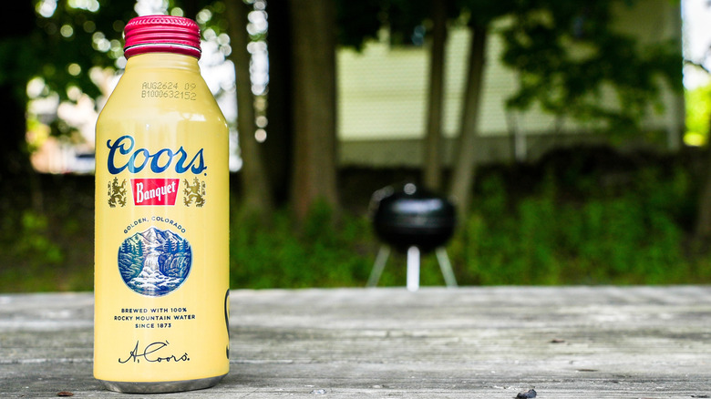 Can of Coors Banquet on picnic table with grill blurred in background