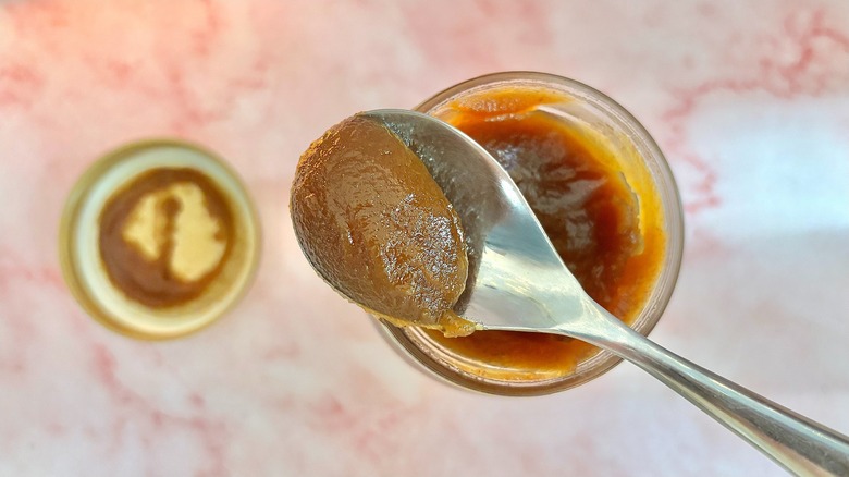 Spoonful of apple butter held above jar of apple butter on pink table
