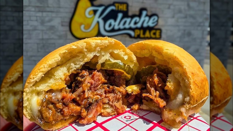 Two halves of shredded meat-filled kolache on tray outside in front of store sign