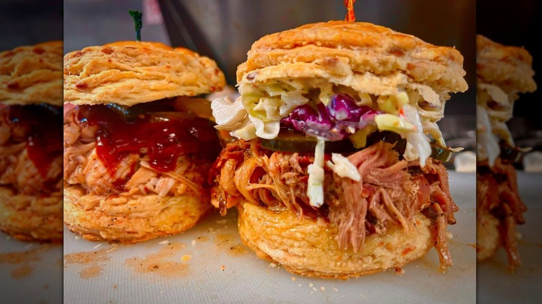Two biscuit sandwiches piled high with pulled pork and coleslaw and dripping with barbecue sauce