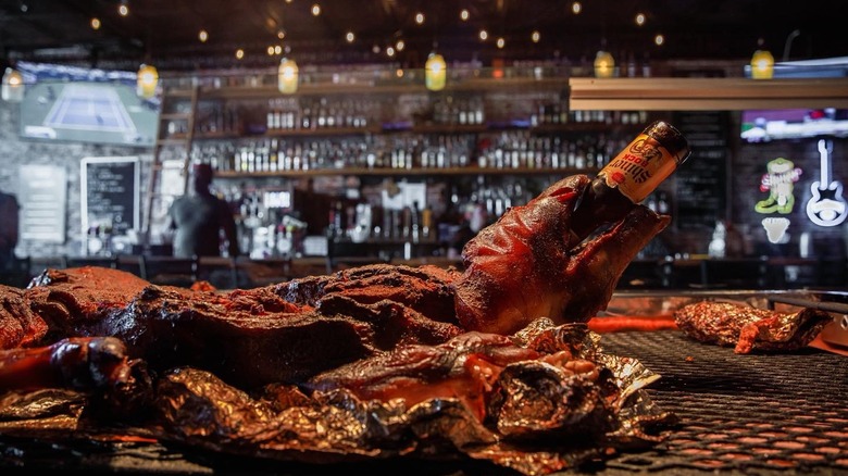 Bottle of Shiner beer sticking out of what may be a pig snout on a platter containing loads of barbecued meats