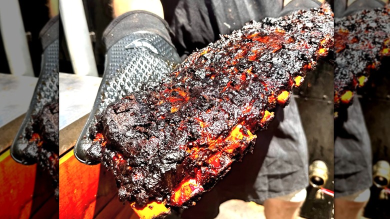 Gloved hands holding up a giant rack of charred ribs