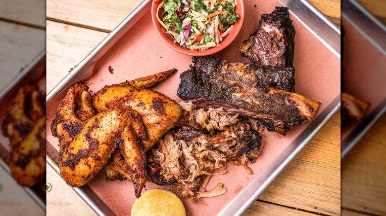 Barbecue meat platter on silver tray featuring chicken wings, pulled pork, and nicely charred ribs, plus a small cup of coleslaw