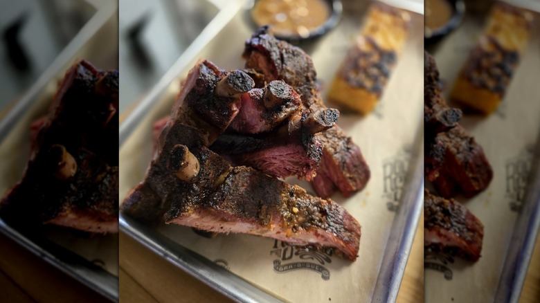 Half slab of nicely crusted ribs on silver tray with what looks like cornbread slice and baked beans in the background