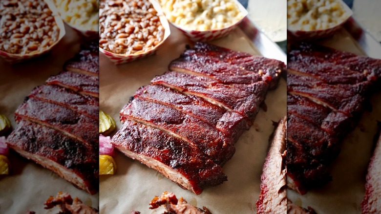 Glazed cherry-smoked ribs sliced on butcher's paper with containers of baked beans and mac and cheese in the background
