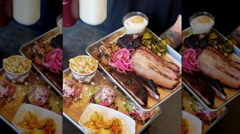 BBQ platter featuring sliced brisket, pickled red onions, brisket tacos, mac and cheese, pulled pork, spare ribs, and banana pudding cup