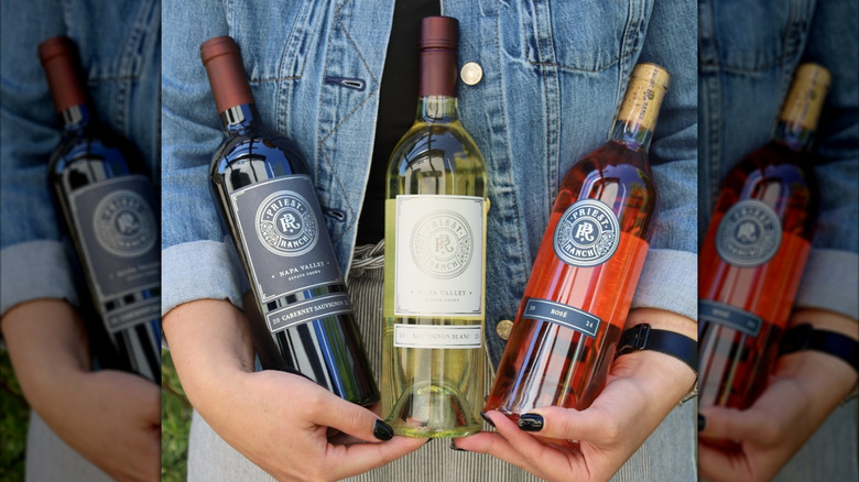 hands holding three wine bottles