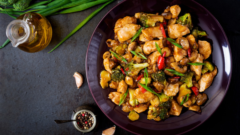 Chinese stir fry dish in black bowl next to oil jug and vegetables