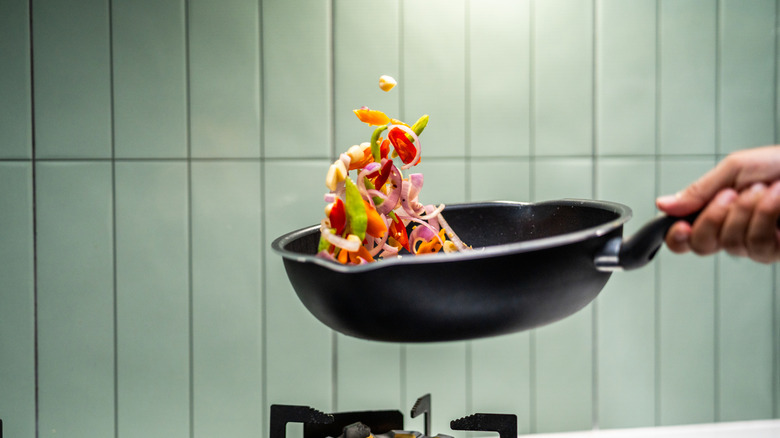 close up of hand flipping vegetables in wok