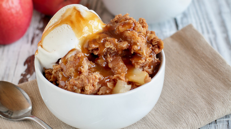 Apple crisp in white bowl with vanilla ice cream