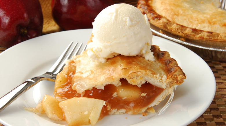 Apple pie with a huge scoop of ice cream on white plate