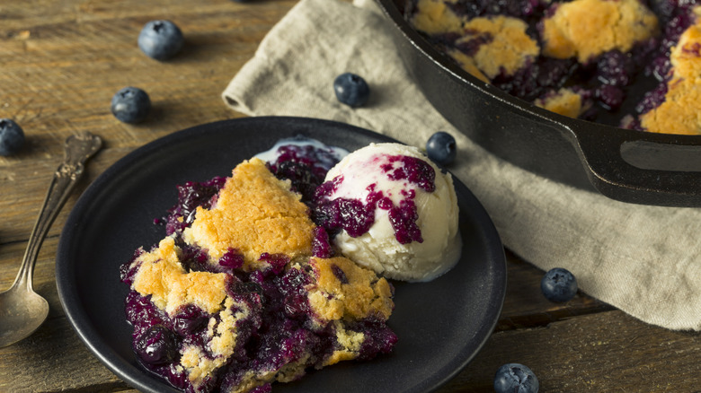 blueberry cobbler serving on a plate with vanilla ice cream and some fresh bluberries