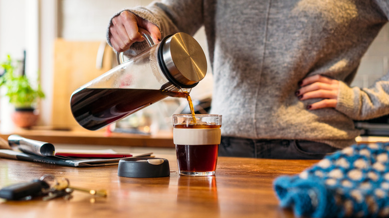 Woman pouring cold brew coffee into a glass on a kitchen countertop