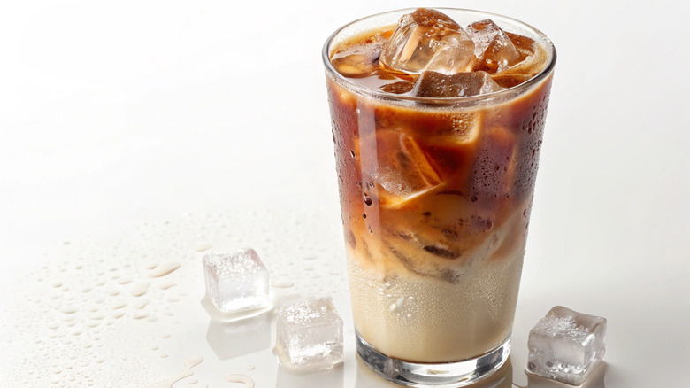A glass of iced coffee with ice melting on the countertop