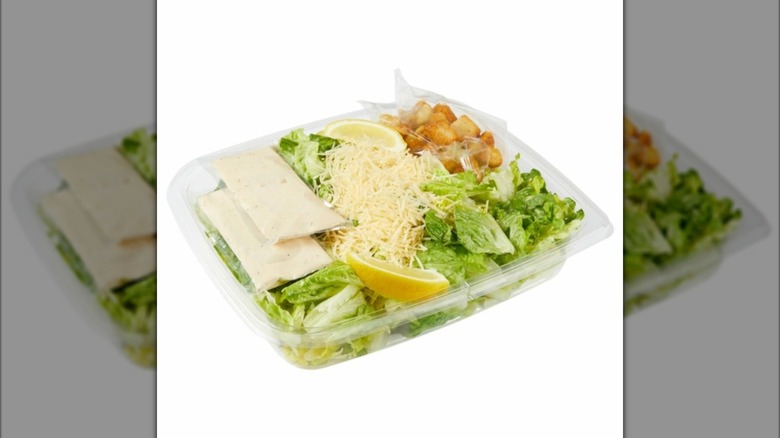 Plastic tray of Kirkland Signature Caesar Salad with dressing packets