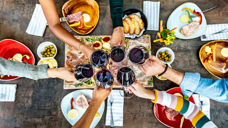 Friends cheering with wine glasses over a dinner table