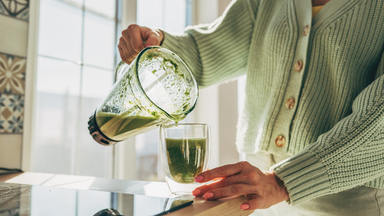 Cold green smoothie in a blender being poured into a glass