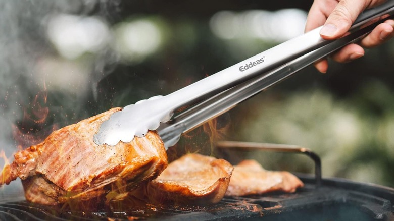 Eddeas Grill Tongs being used to pick up meat off the grill