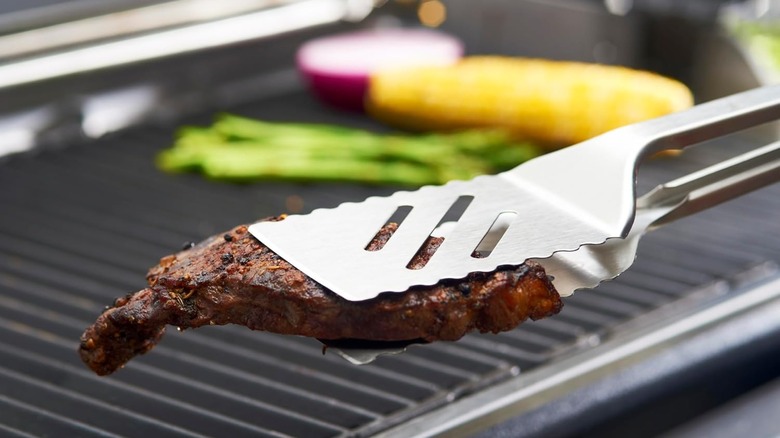 GrillPro 16-inch Tong/Turner Combination holding meat above grill surface