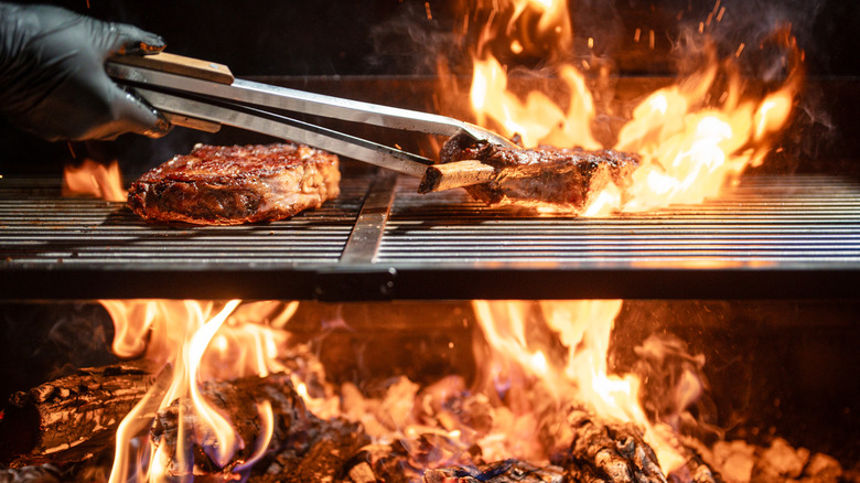 View above and below a grill grate with hand using tongs to place meat