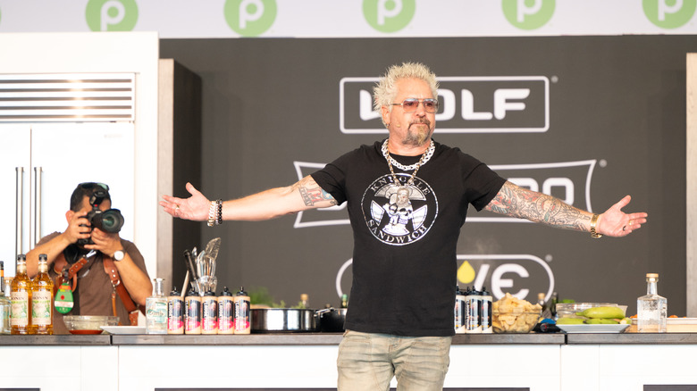 Guy Fieri with his harms held wide on stage during a festival