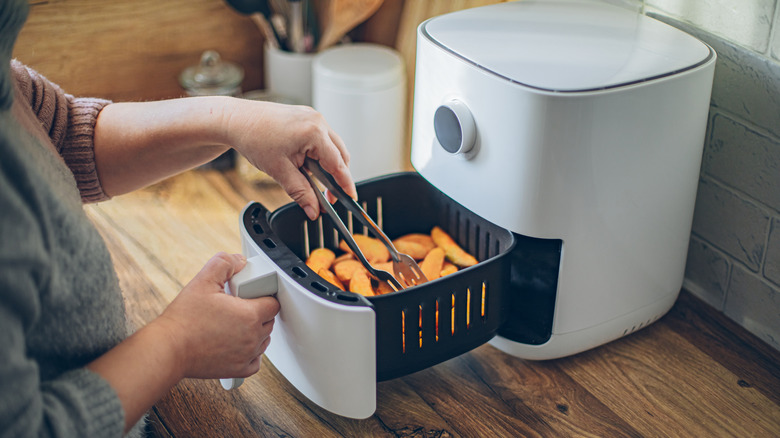 A person placing potato wedges in the basket of a white air fryer